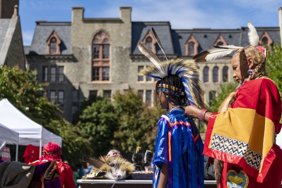 Older woman places a feathered war bonnet on top of a younger boy’s head during ceremony.