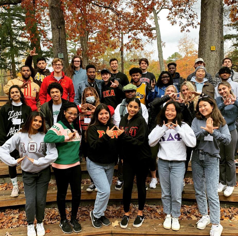 Intercultural Greek Council members pose together outside for a group photo. They are each wearing sweaters with their individual Greek life affiliation.