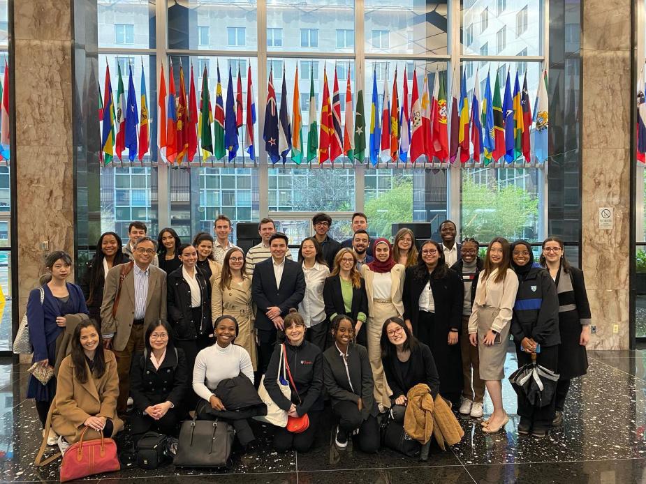 Penn World Scholars students stand together in a lobby area in front of a large display of international flags.