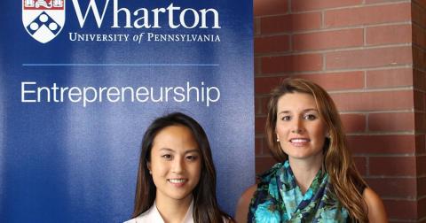 Two Penn alums in front of a Wharton banner