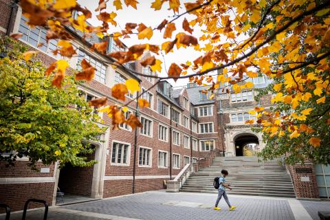 Student walking through Penn's Quad with Fall foliage