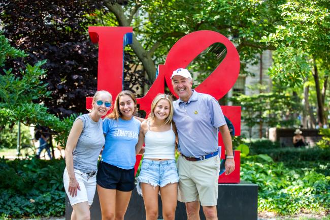 A family of four is posing in front of the LOVE sculpture at the University of Pennsylvania. They’re all smiling, with the parents on the ends and two young women in the middle.