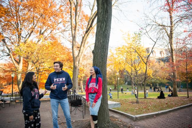 Three students in Penn sweatshirts stand outside having a conversation.