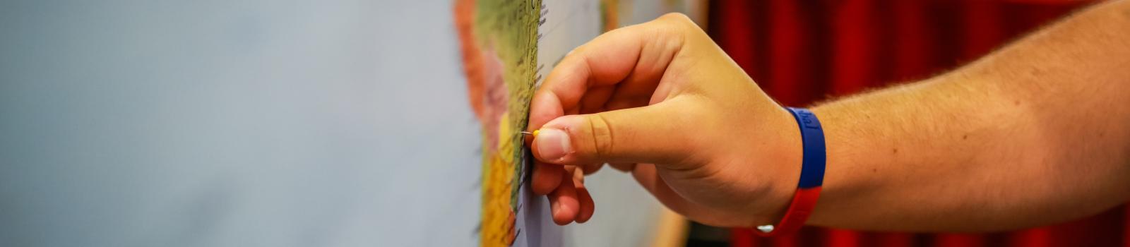 Close-up of hand putting a pin in a wall map of the world