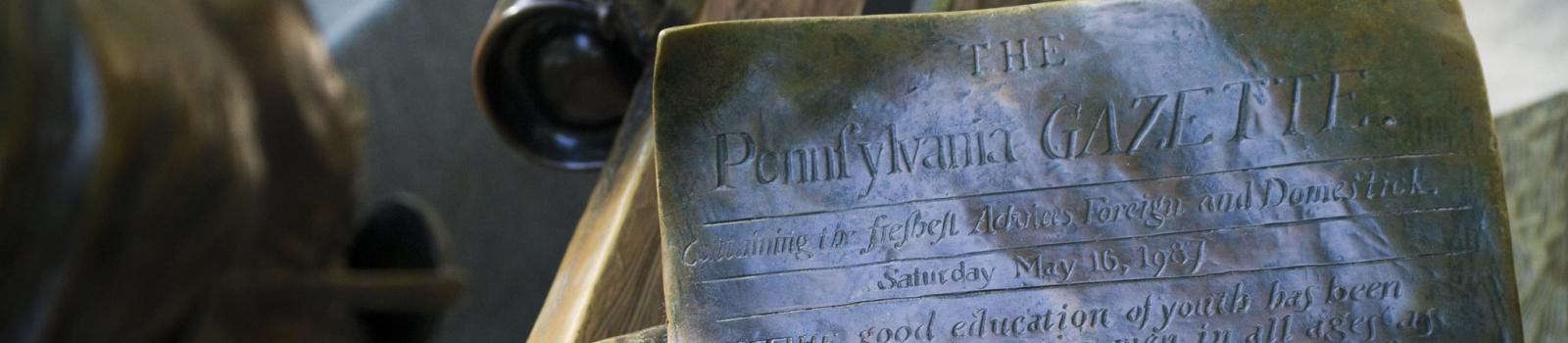 Close-up of Ben Franklin bench statue holding the Pennsylvania Gazette