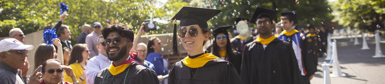 Smiling students walking at graduation with bubbles in the air