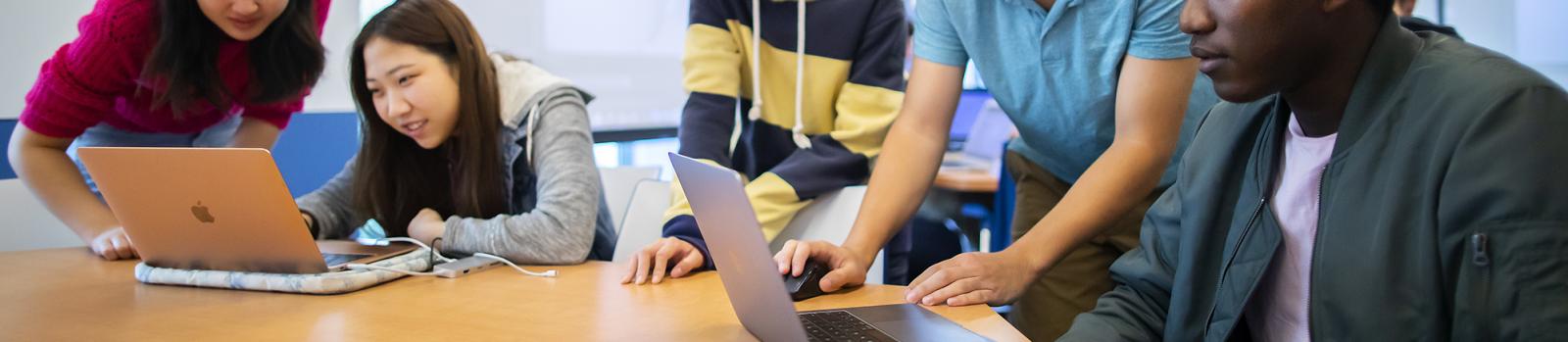 Students at a table looking at laptops together