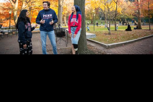 Three students in Penn sweatshirts stand outside having a conversation.