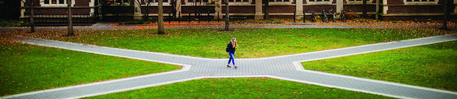Penn student stands in the middle of path intersecting with other walkways. 
